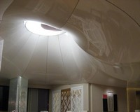 Купольный натяжной потолок из белой глянцевой пленки выполнен плавными линиями.